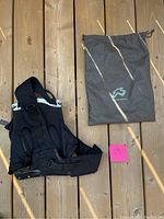 Motorcycle Boblbee safety backpack with shoulder straps and gray storage bag laid flat on wooden floor. Pink note with number 29 included.