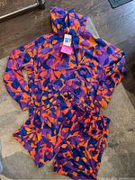 Full set: Men's Nike pullover hoodie and matching shorts, both with abstract multicolor pattern in purple, orange and blue, laid flat on carpet.