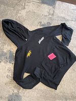 Full front view of black Off White hoodie with front pocket and small orange and white logos on chest.