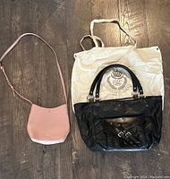 Both purses laid out on wood floor; pink Samara crossbody bag on left, black Ralph Lauren handbag on right with dust bag beneath