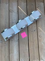 Vanity light fixture laid flat on a wooden surface showing three cylindrical frosted glass light covers with chrome accents around base and edges. A pink numbered tag (13) is beside fixture.