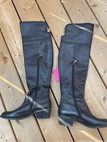 Pair of black leather over-the-knee boots by Vince Camuto laid flat on a wooden surface, showing full side profile including heel and zipper details.