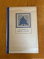 Front cover of the book showing the title "Is There A Santa Claus?" with a stylized blue pine tree graphic and blue spine.