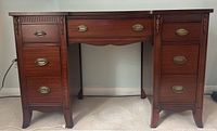 Front full view of antique mahogany desk showing two banks of drawers with brass hardware and decorative carved details.