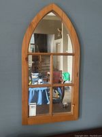 Front view of antique pine cathedral style window mirror hanging on a wall reflecting a room.