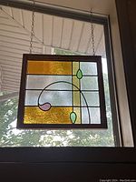 Front view of stained glass panel showing amber, clear, green and purple textured glass with wooden frame and hanging chains.