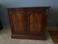 Front view of antique walnut cabinet showing two paneled doors with carved leaf details on vertical edges and ornate handles.