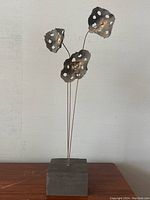 Full front view of the abstract metal flowers sculpture on wooden surface against plain wall background.