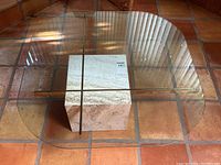 Overhead shot of entire table showing clover-shaped clear glass top and travertine cube base on tiled floor.