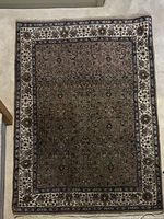 Full view of Persian hand knotted area rug laid flat on a beige carpet, showing detailed floral and ornamental patterns with a cream border.