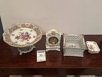 Full view of the 6-piece lot including the floral cake pedestal dish, small clock, box, and two small trays placed on a dark wooden surface.