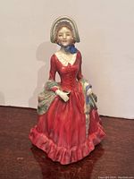 Front view of Royal Doulton porcelain figurine depicting a woman in a red dress and bonnet, holding a small book.