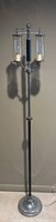 Full view of the tall antique standing lamp with metal and chrome base, black pole, and two glass light fixtures with candle-style bulbs inside.