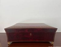 Front view of the jewelry box showing the hand tooled gold decoration, keyhole, and brass claw feet.