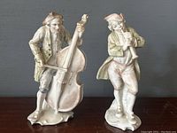 Front-on view of both porcelain figurines side by side on wood surface against gray backdrop