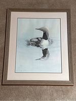 Full view of the signed Glen Loates loon print featuring a loon with chicks, in a light gray wood frame with cream mat.
