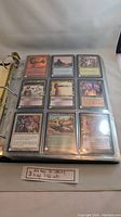 Binder page showing nine Magic The Gathering cards in individual sleeves, including diverse colored card backs and fantasy art.