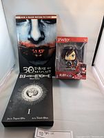 Front view of the lot including 30 Days of Night item, Death Note Black Edition manga, and RWBY Ruby Rose figurine in box.