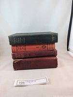 Stack of four antique hardcover books with varying colored cloth covers showing wear, titles partially visible