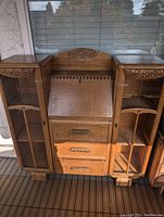 Full view of the antique oak wood bookcase showing two glass door cabinets, drop-down writing desk center, and three carved handle drawers below.