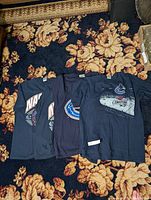 Four navy blue Vancouver Canucks t-shirts laid out sequentially on a floral carpet.
