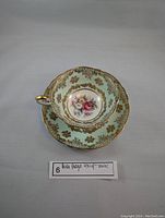Close-up of teacup placed inside saucer showing gold and mint green floral design with floral center.