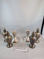 Full lot showing two pairs of salt and pepper shakers and two candle sticks arranged in a semi-circle
