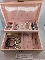 Jewelry box with contents spread between top and bottom compartments, including multiple bracelets, necklaces, and charms