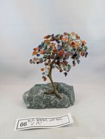 Front view of multi-colour gemstone tree with gold wire trunk mounted on green natural stone base, showing the dense arrangement of gemstone chips.