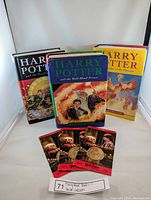 Three Harry Potter hardcover books upright, with covers visible: Order of the Phoenix, Half-Blood Prince, Deathly Hallows, plus three Unum Gringotts Galleon coins in packaging in front.