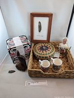 Wide view of entire lot showing Navajo figurine, framed feather art, woven basket, ceramic mugs, wooden bird carving, and arrowhead on woven tray