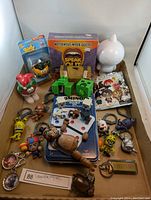 Overall box contents showing Speak Out game, dominoes, multiple key chains and figures, wooden treasure chest, and white cat figure