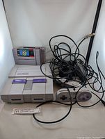 Full view of SNES console with two cartridges inserted, wired controller, and tangled cables