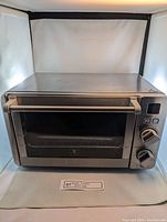 Front view of the toaster oven showing the glass door, handle, control buttons, and dials.