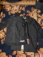 Two black women's jackets laid flat on floral carpet: Swiss Tech jacket on left with hood and zipper, Addition Elle long coat on right.