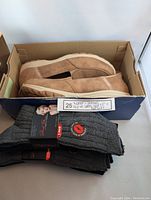 Photo showing brown Skechers slip-in loafers in box along with two sets of gray Marilyn Monroe branded boot socks stacked alongside.