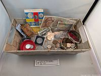 Basket containing various world coins, banknotes, silver coins in holders, and a currency conversion chart.