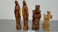 Photo showing all four wood carving figurines side by side against a plain background.