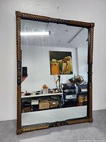 Front view of antique Italian wall mirror showing carved gold gilt frame with leaf and rosette details reflecting workshop interior.
