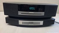 Front view of Bose Wave Music System stacked atop 4-CD changer accessory with digital clock display illuminated