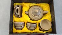 Top-down photo of the small Chinese clay tea set including teapot, six cups, and six matching saucers, all housed in a black box with yellow fabric lining.