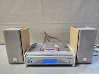 Front view of JVC CA-FSSD550 compact component system with two wooden speakers and remote on top. Shows system in working state with disc spinning visible through transparent cover.