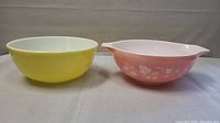 Front view of two PYREX bowls side by side: pink Gooseberry Cinderella bowl with handles and yellow mixing bowl