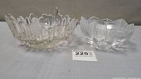 Lot of two glass bowls on a gray surface. Larger irregular jagged ice glass bowl on left, smaller petal shaped glass bowl on right.
