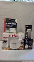 Four kitchen items including T-Fal fryer box, Black & Decker can opener box, cheese grater and salt pepper shakers.