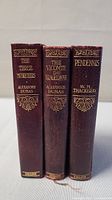 Photo of three vintage books spines showing titles (The Three Musketeers, The Vicomte de Bragelonne, Pendennis) with embossed gold lettering on maroon covers.