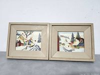 Front view of two framed paint by number winter landscape village paintings, showing both pieces side by side.