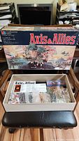 Full game box with vintage Axis & Allies artwork and contents inside box on a chair.