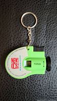 Front view of green plastic key chain viewer with circular image disc labeled New Kids On The Block and key ring attached.