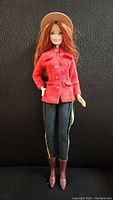 Front view of Barbie RCMP doll, showing red uniform jacket, black pants with yellow stripes, brown boots, and beige RCMP hat.